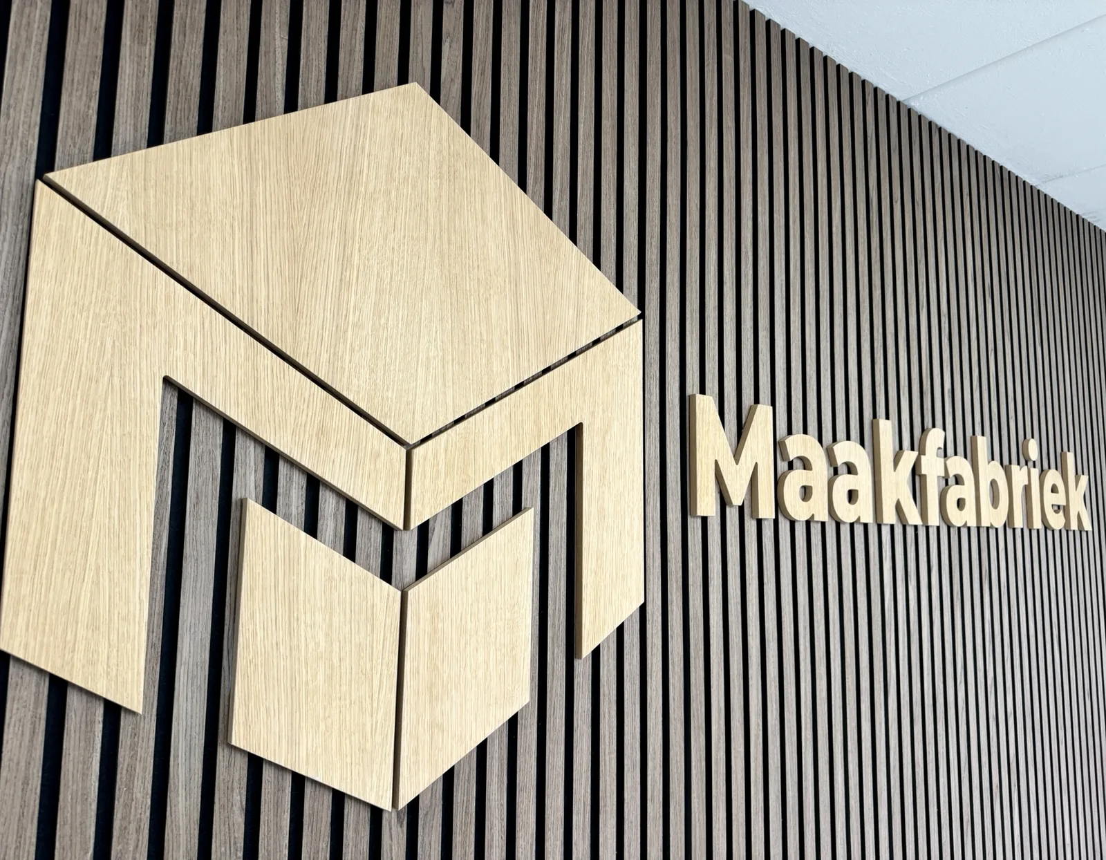 Het logo van Maakfabriek in eiken op een lamellenwand